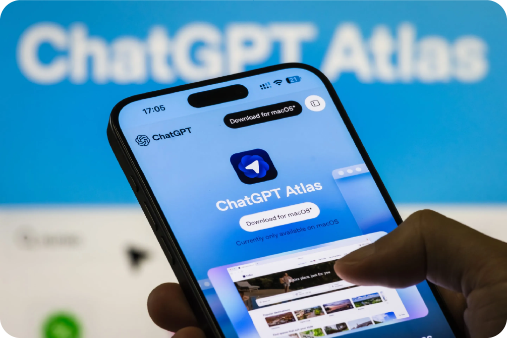 Hand holding smartphone displaying ChatGPT Atlas AI browser interface for macOS.