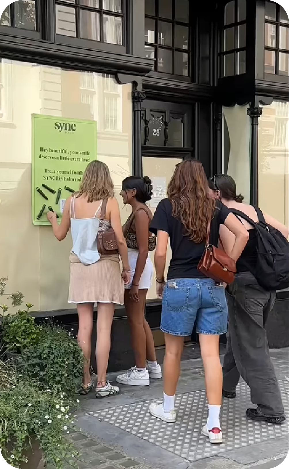 Pedestrians interacting with a Sync Beauty street poster in London to peel off free lip balm samples, illustrating an interactive guerilla marketing campaign.